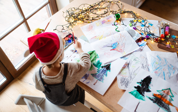 Top view of unrecognizable small child indoors at home at Christmas, painting pictures with waterpaints.