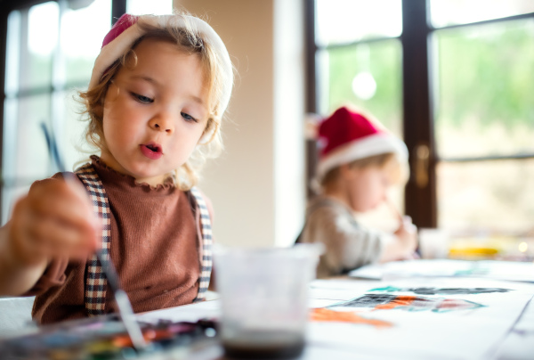 Portrait of happy small girl and boy indoors at home at Christmas, painting pictures.