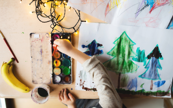 Top view of unrecognizable small child indoors at home at Christmas, painting pictures with waterpaints.