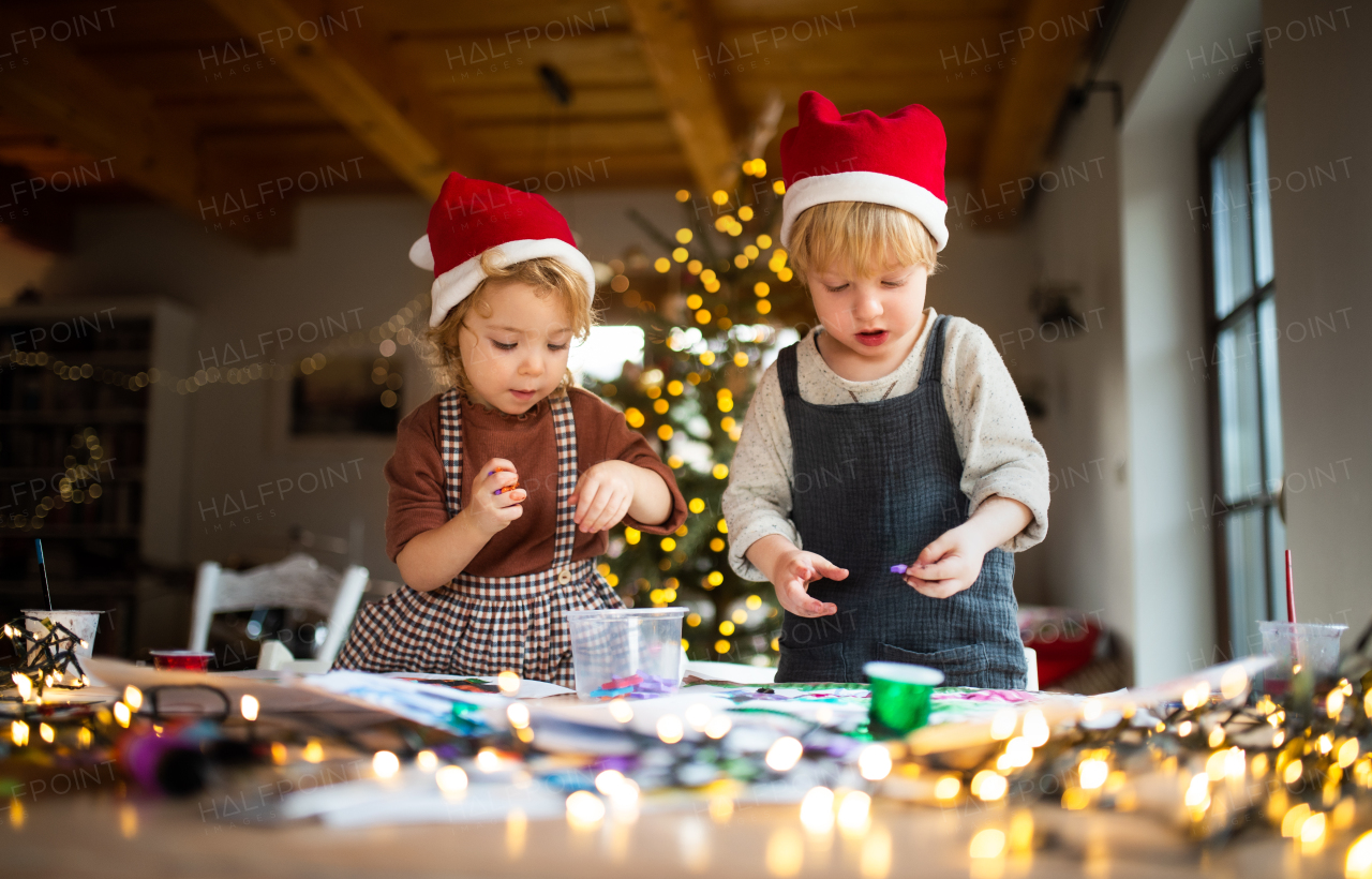 Portrait of happy small girl and boy indoors at home at Christmas, doing art and craft.