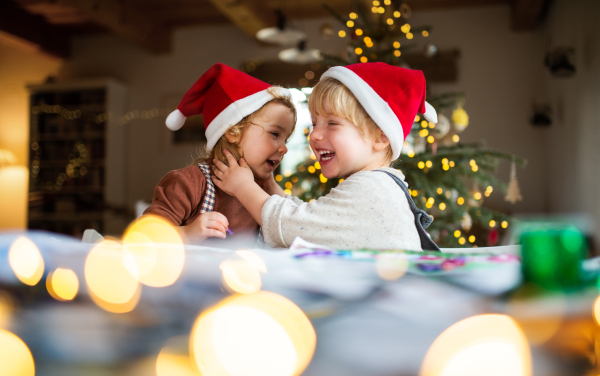 Portrait of happy small girl and boy indoors at home at Christmas, having fun.