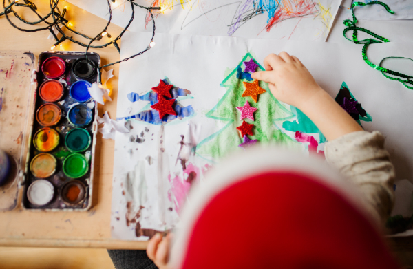 Top view of unrecognizable small child indoors at home at Christmas, painting and decorating pictures.