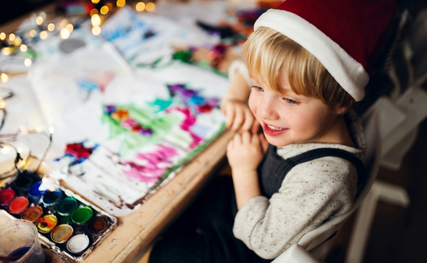 Top view of happy small boy indoors at home at Christmas, painting pictures.