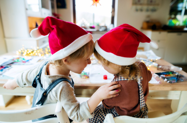 Rear view of small girl and boy indoors at home at Christmas, having fun when painting pictures.