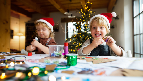 Portrait of happy small girl and boy indoors at home at Christmas, doing art and craft.