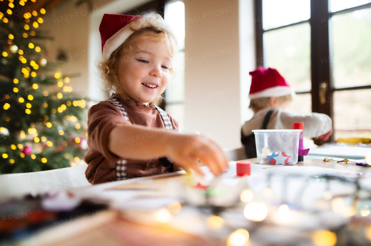 Portrait of happy small girl and boy indoors at home at Christmas, painting pictures.