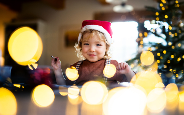 Portrait of happy small girl indoors at home at Christmas, painting pictures.