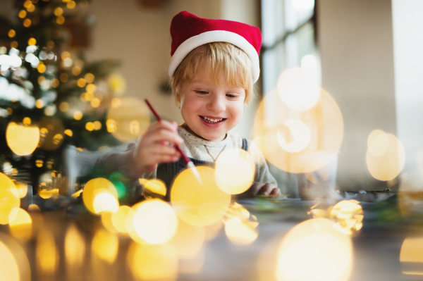 Portrait of happy small boy indoors at home at Christmas, painting pictures.