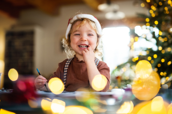 Portrait of happy small girl indoors at home at Christmas, painting pictures.