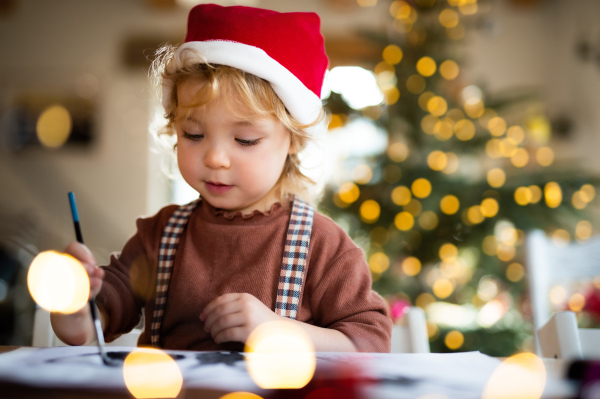 Portrait of happy small girl indoors at home at Christmas, painting pictures.