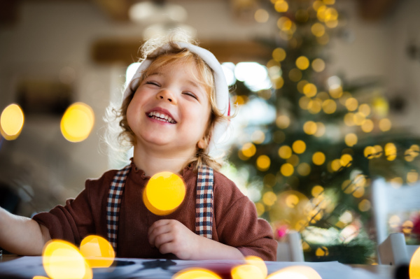 Portrait of happy small girl indoors at home at Christmas, laughing.