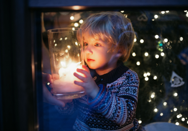 Portrait of happy small boy indoors at home at Christmas, holding candle at night.