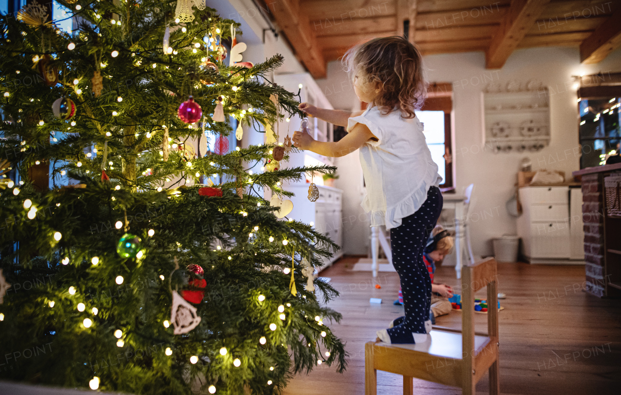 Side view portrait of small girl indoors at home at Christmas, decorating tree.