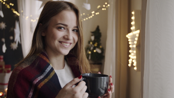 Portrait of happy young woman indoors at home at Christmas, holding cup of coffee.