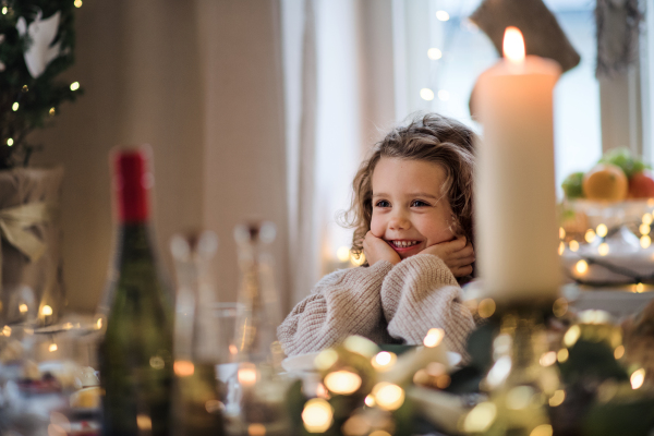 Happy small girl sitting at the table indoors at Christmas, laughing.