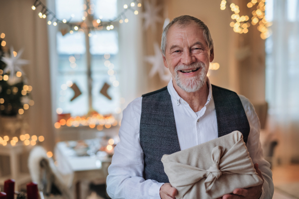 Front view of happy senior man indoors holding present at Christmas, looking at camera.