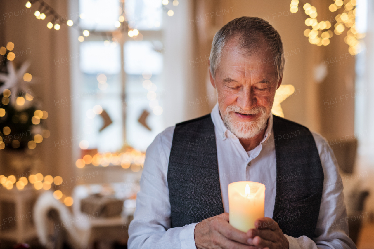 A front view of happy senior man indoors holding candle at Christmas.