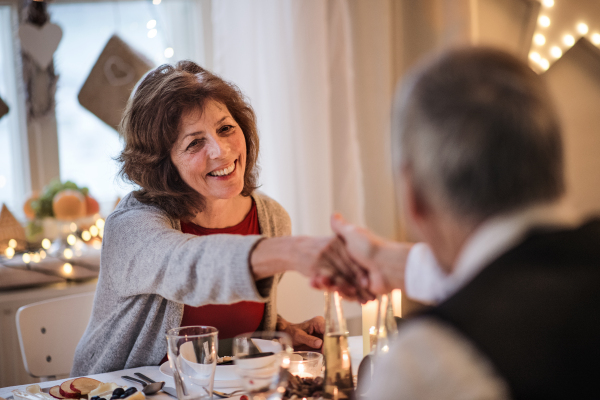 Portrait of happy senior couple in love indoors at home sitting at the table at Christmas, talking.