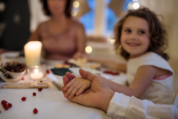 Small girl with family sitting indoors celebrating Christmas together, praying at the table.