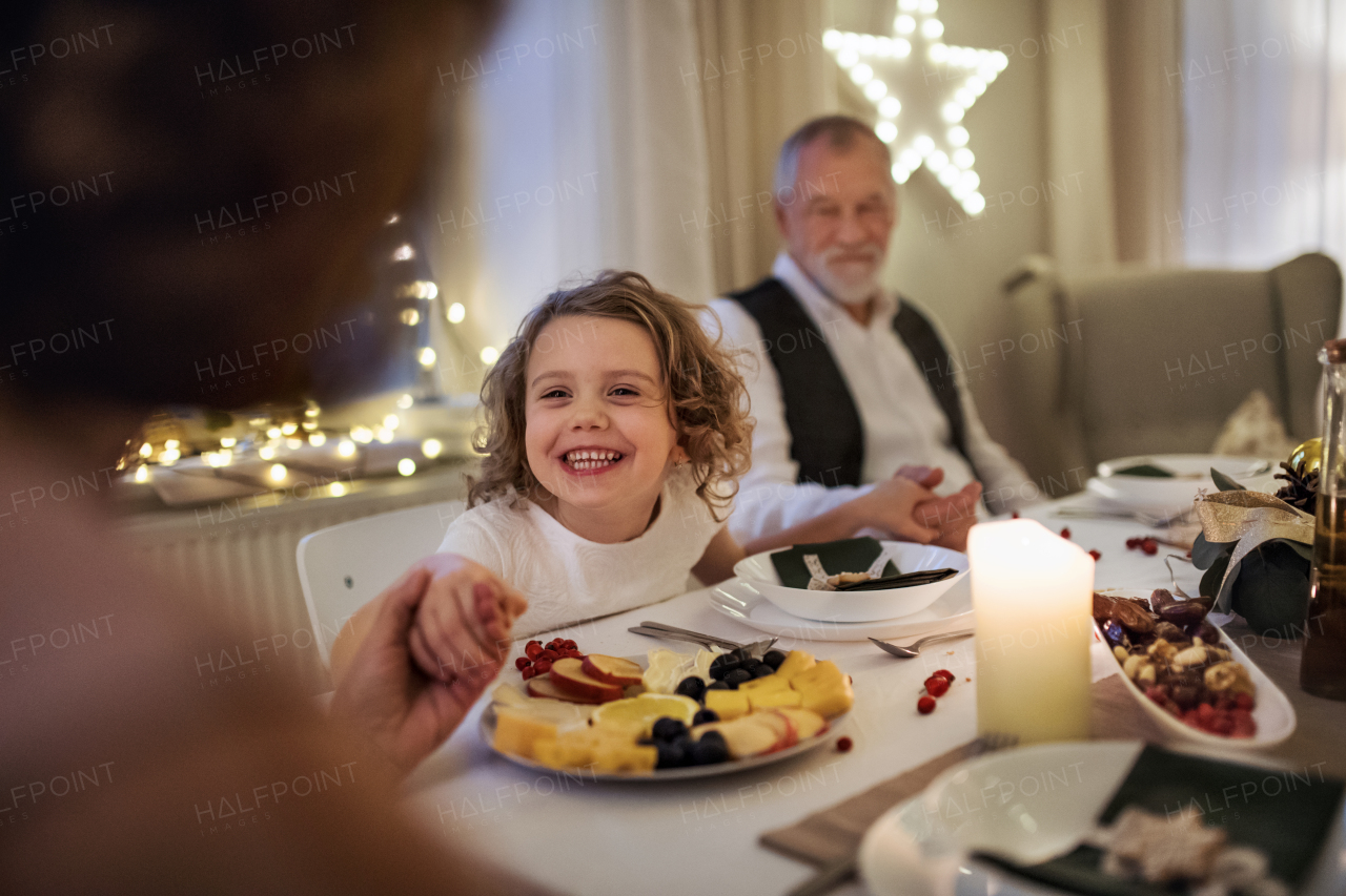 Happy small girl with grandparents sitting indoors celebrating Christmas together.