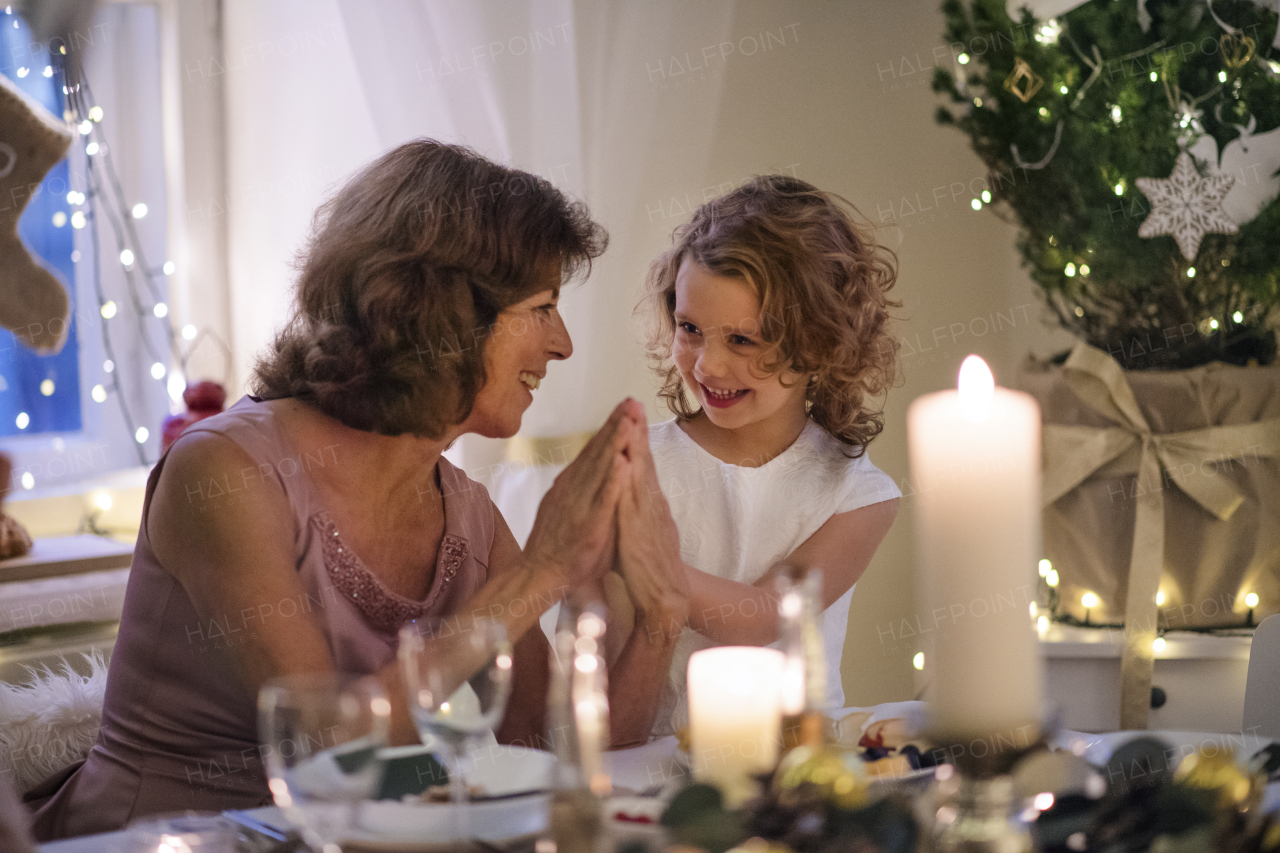 Senior woman with small granddaughter indoors at Christmas, having fun.