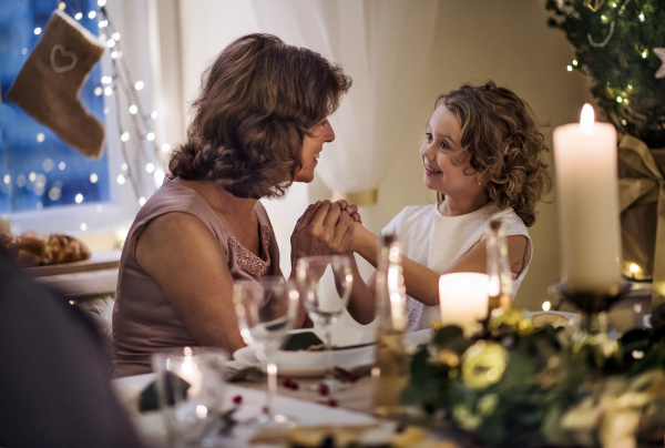 Senior woman with small granddaughter indoors at Christmas, talking.