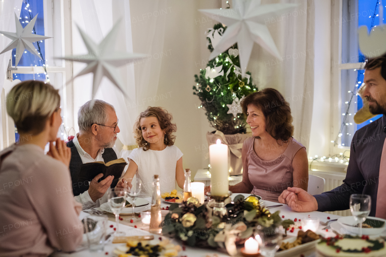 Small girl with parents and grandparents indoors celebrating Christmas, reading Bible.