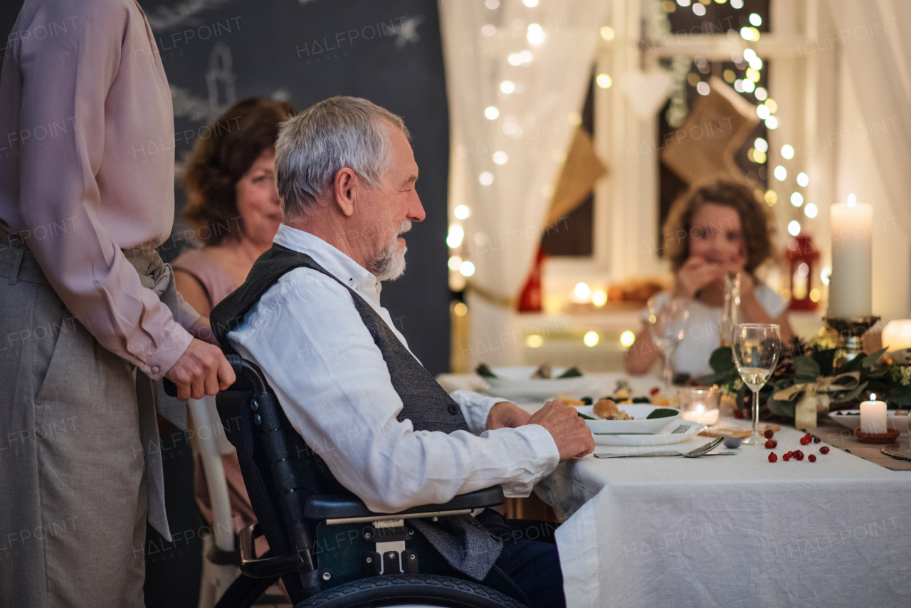 Happy senior man in wheelchair with family indoors celebrating Christmas together.