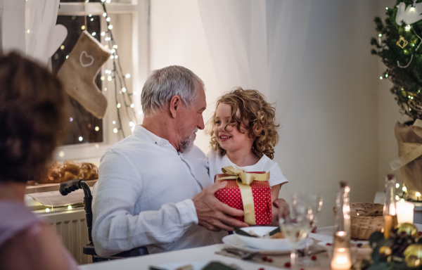 Happy senior man in wheelchair with family indoors celebrating Christmas together.