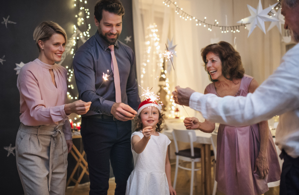 Small girl with parents and grandparents indoors celebrating Christmas, holding sparklers.