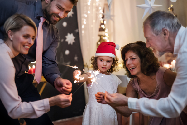 Portrait of small girl with parents and grandparents indoors celebrating Christmas, holding sparklers.