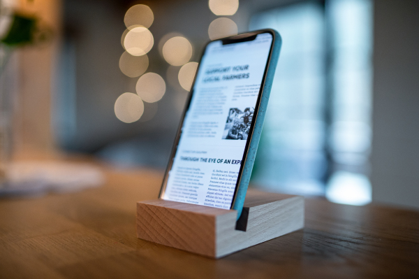 A smartphone in wooden stand holder on table indoors at home or on office.