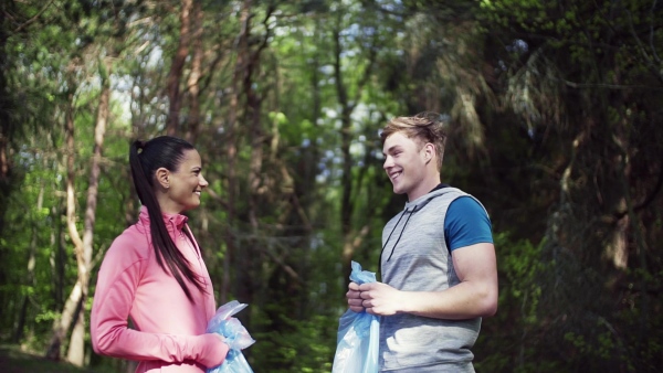 A group of fit young people picking up litter in nature, a plogging concept. Slow motion.