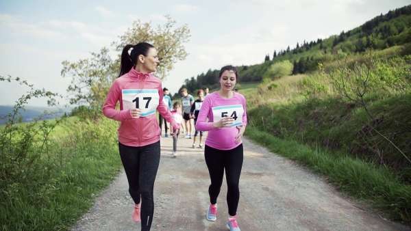 Pregnant woman with group of multi generation people running a race competition in nature. Slow motion.