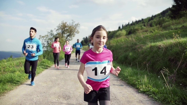 A large group of active multi generation people running a race competition in nature. Slow motion.