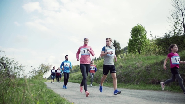 A large group of active multi generation people running a race competition in nature. Slow motion.