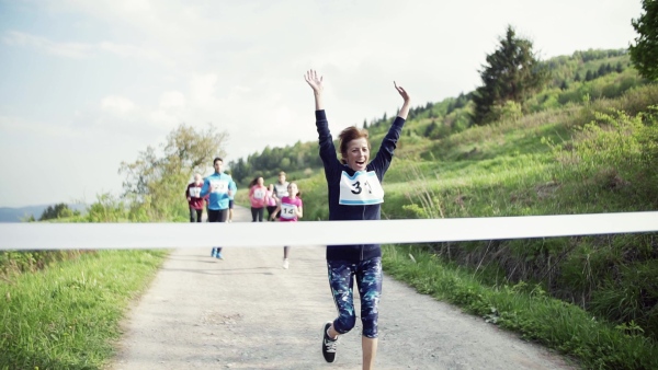 A senior woman runner crossing finish line in a race competition in nature.Slow motion.