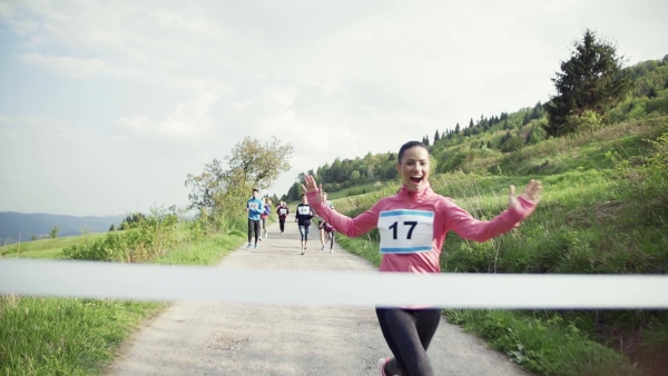 A young woman runner crossing finish line in a race competition in nature. Slow motion.