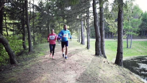 A large group of active multi generation people running a race competition in nature. Slow motion.