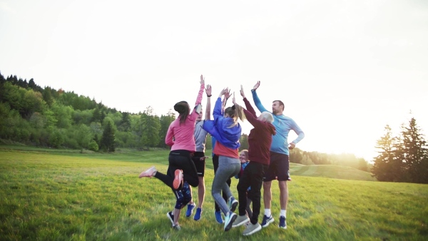 A large group of fit and active people jumping after doing exercise in nature. Slow motion.