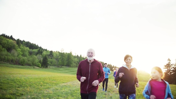 A large group of people cross country running in nature at sunset. Slow motion.