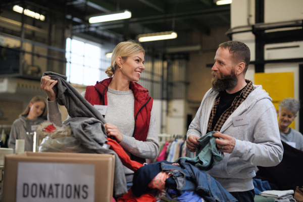 Portrait of volunteers sorting out donated clothes in community charity donation center.