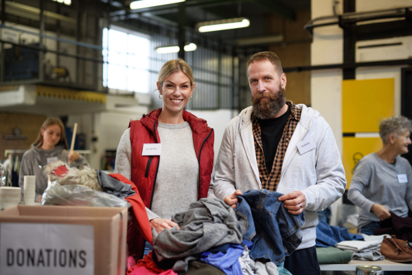 Portrait of volunteers sorting out donated clothes in community charity donation center.