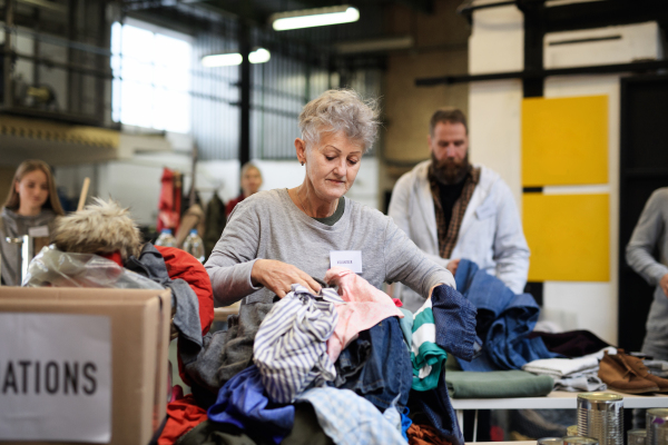 Portrait of volunteers sorting out donated clothes in community charity donation center.