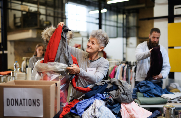 Portrait of volunteers sorting out donated clothes in community charity donation center, coronavirus concept.