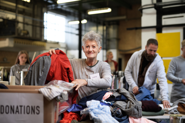 Portrait of volunteers sorting out donated clothes in community charity donation center.