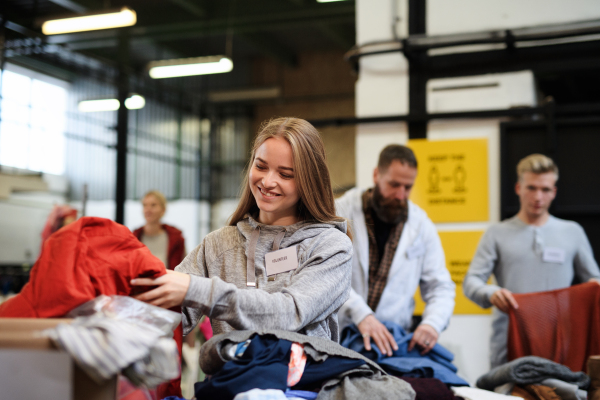 Portrait of volunteers sorting out donated clothes in community charity donation center.