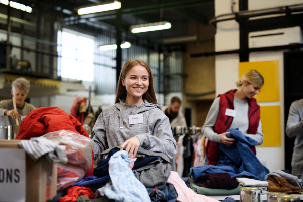 Portrait of volunteers sorting out donated clothes in community charity donation center, coronavirus concept.