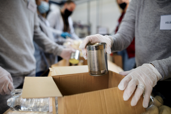 A midsection of group of volunteers in community donation center, food bank and coronavirus concept.