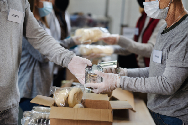 Group of unrecognizable volunteers working in community charity donation center, food bank and coronavirus concept.